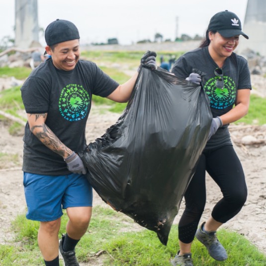 Two FoLAR volunteers carrying a bag of trash