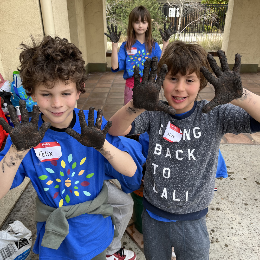 Students hold up their mud covered hands.