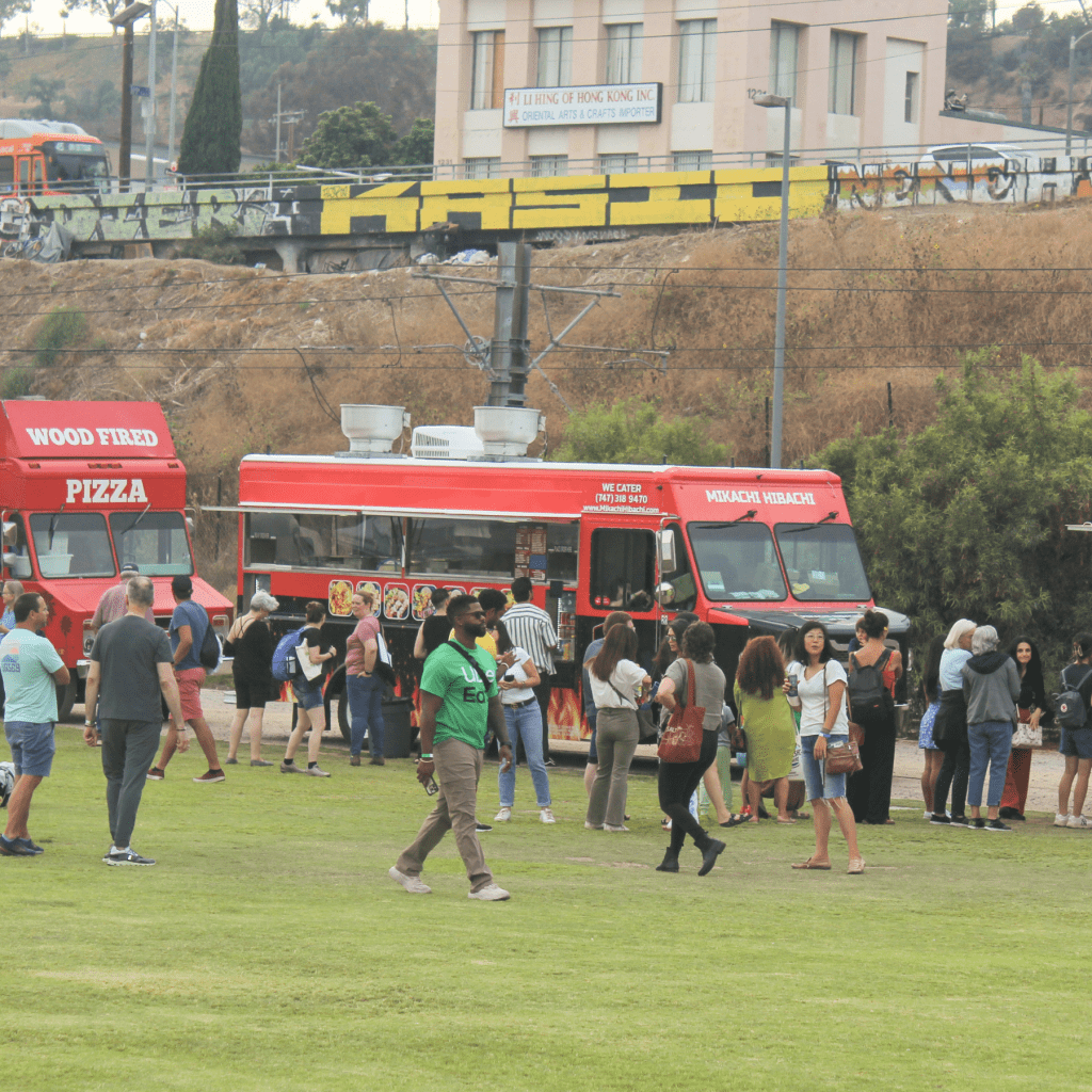 River Fest 2023 attendees order meals at several food trucks parked on the edge of a large grass area at Los Angeles State Historic Park.